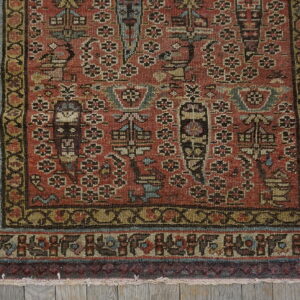 Intricate rust and multi-color patterned rug corner with borders lying on weathered gray wooden planks.