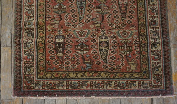 Intricate rust and multi-color patterned rug corner with borders lying on weathered gray wooden planks.