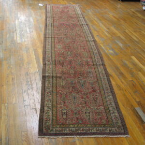 Red runner rug with complex geometric patterns displayed on worn wood plank flooring.