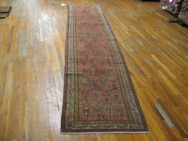Red runner rug with complex geometric patterns displayed on worn wood plank flooring.