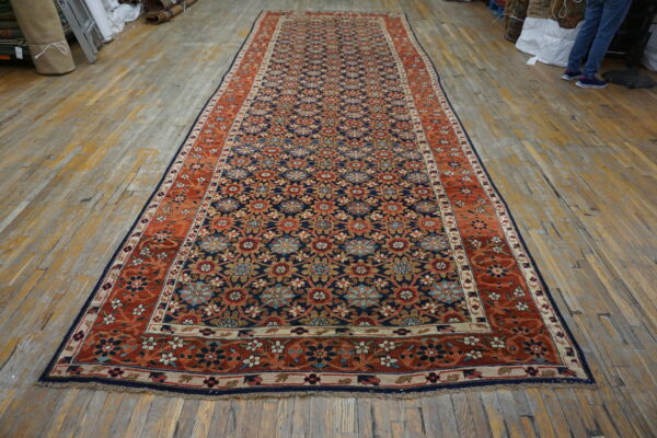 Navy blue runner rug featuring an all-over floral design and rust-colored borders on wood flooring.