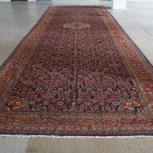 Long low-pile runner rug with a complex red and dark blue medallion pattern on large gray concrete tiles.