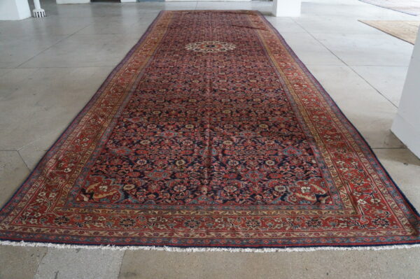 Long low-pile runner rug with a complex red and dark blue medallion pattern on large gray concrete tiles.