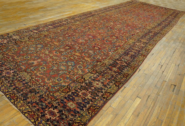 Long runner rug with a dense red, blue, and gold traditional pattern displayed on rustic wood floors.