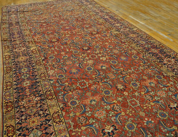 Distressed, low-pile gallery rug with complex red, blue, and gold traditional patterns on wood flooring.