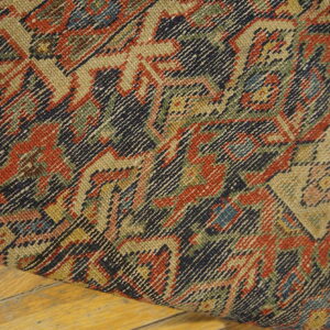 Close-up of a tightly woven rug featuring geometric designs in red, navy, and tan on a wood floor.