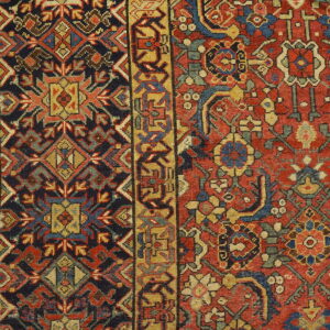 Densely woven rug detail shows geometric red and navy field motifs bordering a gold geometric pattern.