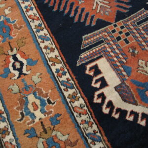 Navy and terracotta patterned rug resting on light wood flooring, showing dense geometric designs.