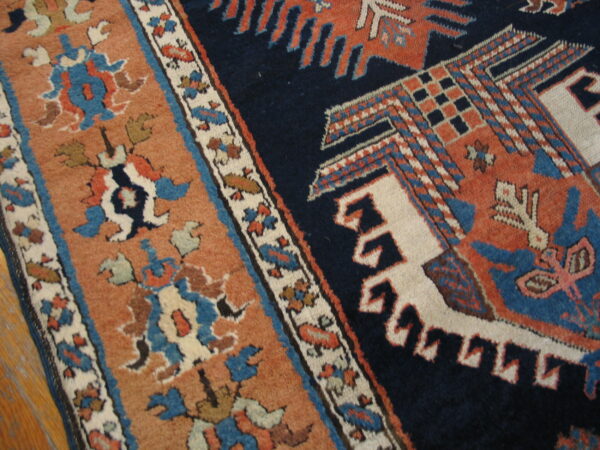 Navy and terracotta patterned rug resting on light wood flooring, showing dense geometric designs.