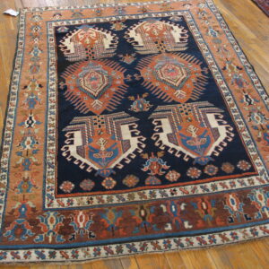 Geometric navy blue and terracotta rug with complex tribal designs displayed on a light wood floor.