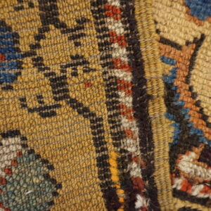 Tight close-up of a low-pile rug with yellow, black, blue, and red traditional geometric designs.