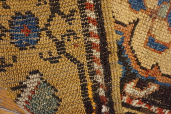 Tight close-up of a low-pile rug with yellow, black, blue, and red traditional geometric designs.