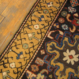 Textured rug with dark brown field and golden floral border rests on distressed wood planks.