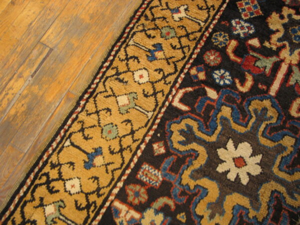 Textured rug with dark brown field and golden floral border rests on distressed wood planks.