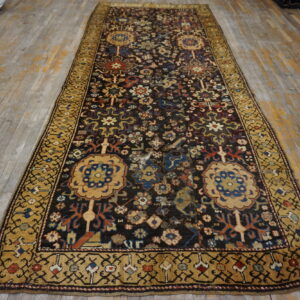 Distressed dark runner rug with detailed floral patterns and a wide gold border on faded wood flooring.