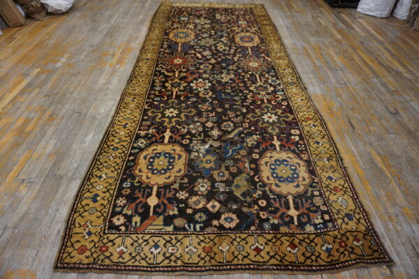 Distressed dark runner rug with detailed floral patterns and a wide gold border on faded wood flooring.