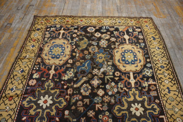 Traditional low-pile rug with a dark field, golden border, and blue and tan patterns on worn wood floors.
