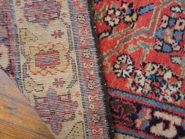 The folded edge of a red, blue, and tan high-pile rug displays its tightly woven backing on wood planks.