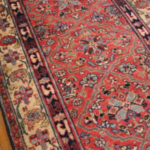 A traditional low-pile rug with red, navy, and beige intricate patterns rests on wood flooring.