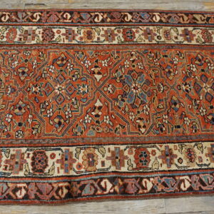 A rust-toned runner rug with intricate blue and cream geometric designs sits on distressed wood plank flooring.