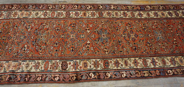 A rust-toned runner rug with intricate blue and cream geometric designs sits on distressed wood plank flooring.