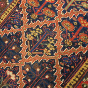 Intricate, low-pile rug pattern featuring rust red and yellow motifs on a dark blue ground.