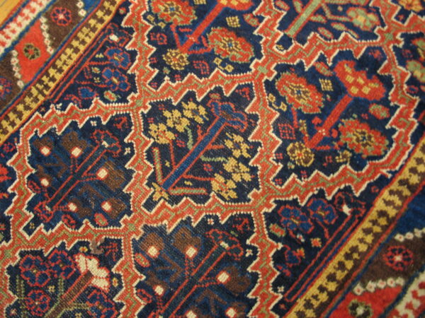 Intricate, low-pile rug pattern featuring rust red and yellow motifs on a dark blue ground.