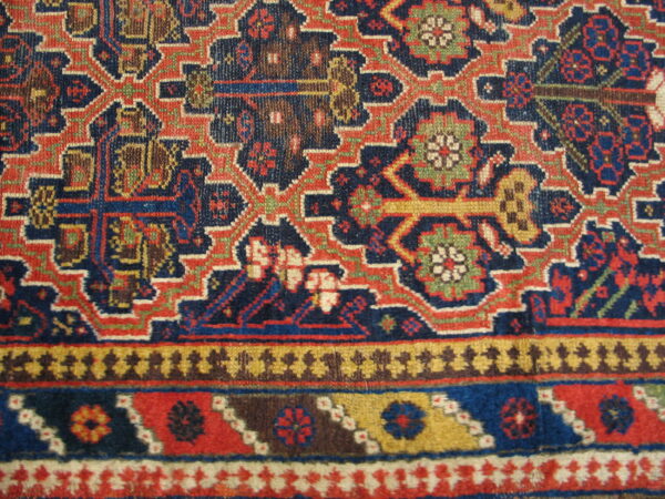 Geometric tribal rug featuring interlocking motifs in navy, red, gold, brown, and green borders.