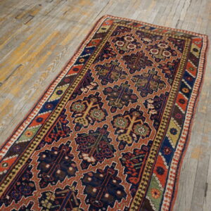 A traditional runner rug with navy, rust, and gold colors lays on distressed, gray-washed wood floors.