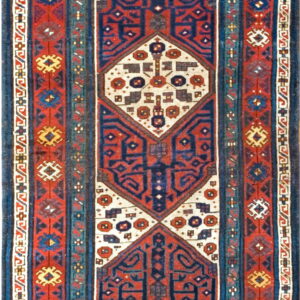 A runner rug with large geometric medallions in navy blue, rust red, and cream colors.