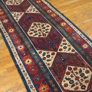 Red, navy, and cream geometric runner rug displayed on light brown wood flooring.