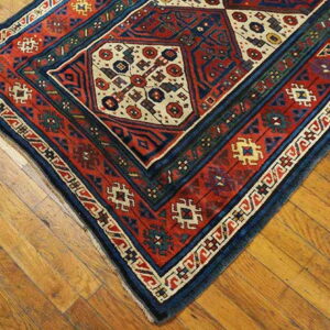 A traditional rug with red, navy, and cream octagonal motifs rests on light brown distressed hardwood floors.