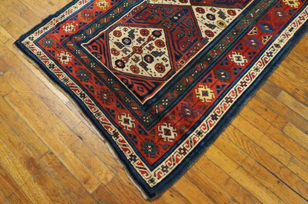 A traditional rug with red, navy, and cream octagonal motifs rests on light brown distressed hardwood floors.