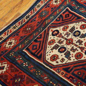 Geometric patterned rug in red, navy, and cream colors rests on light brown wooden floorboards.