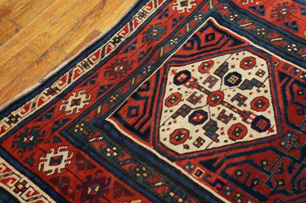 Geometric patterned rug in red, navy, and cream colors rests on light brown wooden floorboards.