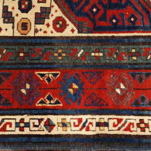 Geometric rug detail showing stacked borders in deep red, navy blue, cream, and dark green.