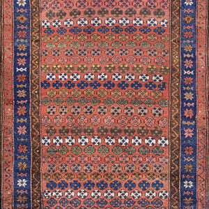 Red rug featuring horizontal rows of repeating multicolored geometric medallions and wide blue floral borders.