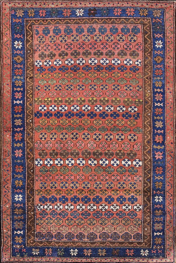 Red rug featuring horizontal rows of repeating multicolored geometric medallions and wide blue floral borders.