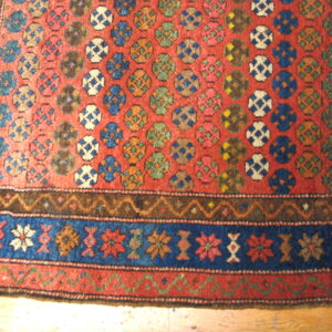 Red rug with repeating blue, green, and white medallion pattern and intricate floral blue borders.