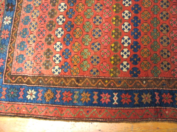Red rug with repeating blue, green, and white medallion pattern and intricate floral blue borders.