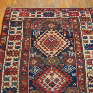 Geometric rug with a navy, red, and cream tribal pattern border resting on natural wood planks.