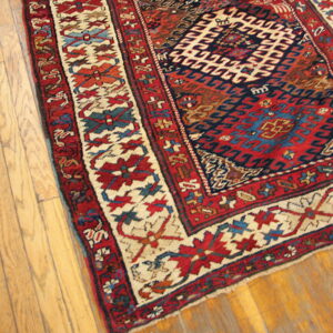 Red, navy, and cream geometric rug with a detailed border placed partially on light brown hardwood planks.