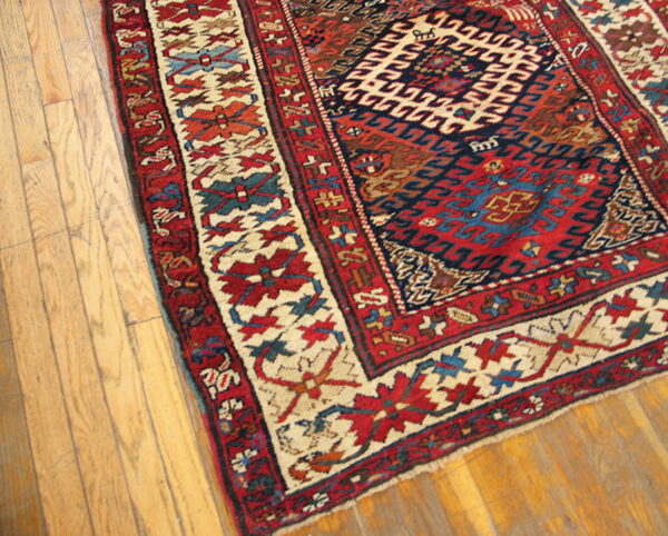 Red, navy, and cream geometric rug with a detailed border placed partially on light brown hardwood planks.