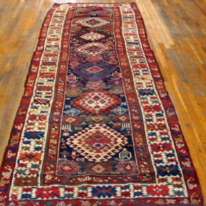 Geometric runner rug with stylized medallions and complex borders in red, blue, and off-white on wood floor.