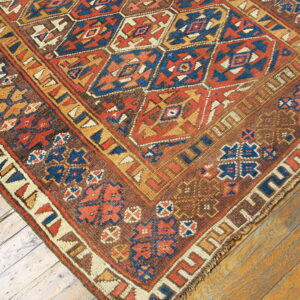 Close-up of a rustic rug featuring red, blue, and brown geometric diamonds over wood planks.