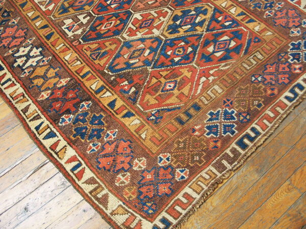 Close-up of a rustic rug featuring red, blue, and brown geometric diamonds over wood planks.
