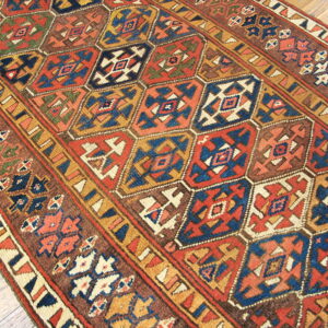 Geometric runner rug with repeating hexagonal shapes in rust, navy blue, gold, and brown on light wood floor.