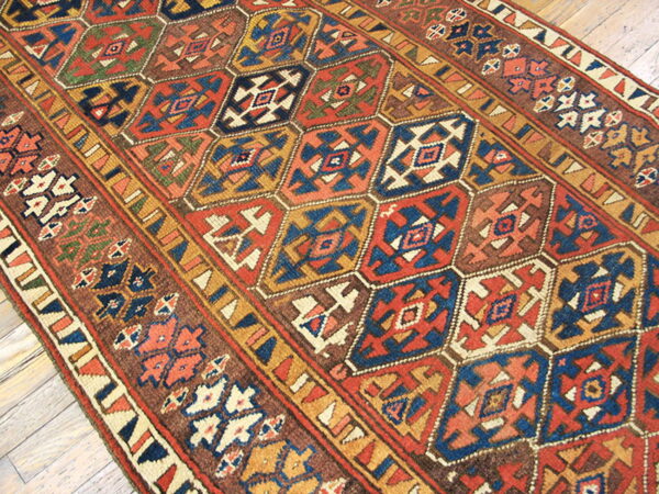 Geometric runner rug with repeating hexagonal shapes in rust, navy blue, gold, and brown on light wood floor.