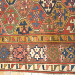 Multicolored geometric rug detail featuring hexagonal shapes, low pile texture, wide borders, and visible wood floor.