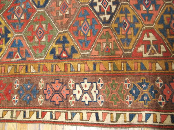 Multicolored geometric rug detail featuring hexagonal shapes, low pile texture, wide borders, and visible wood floor.